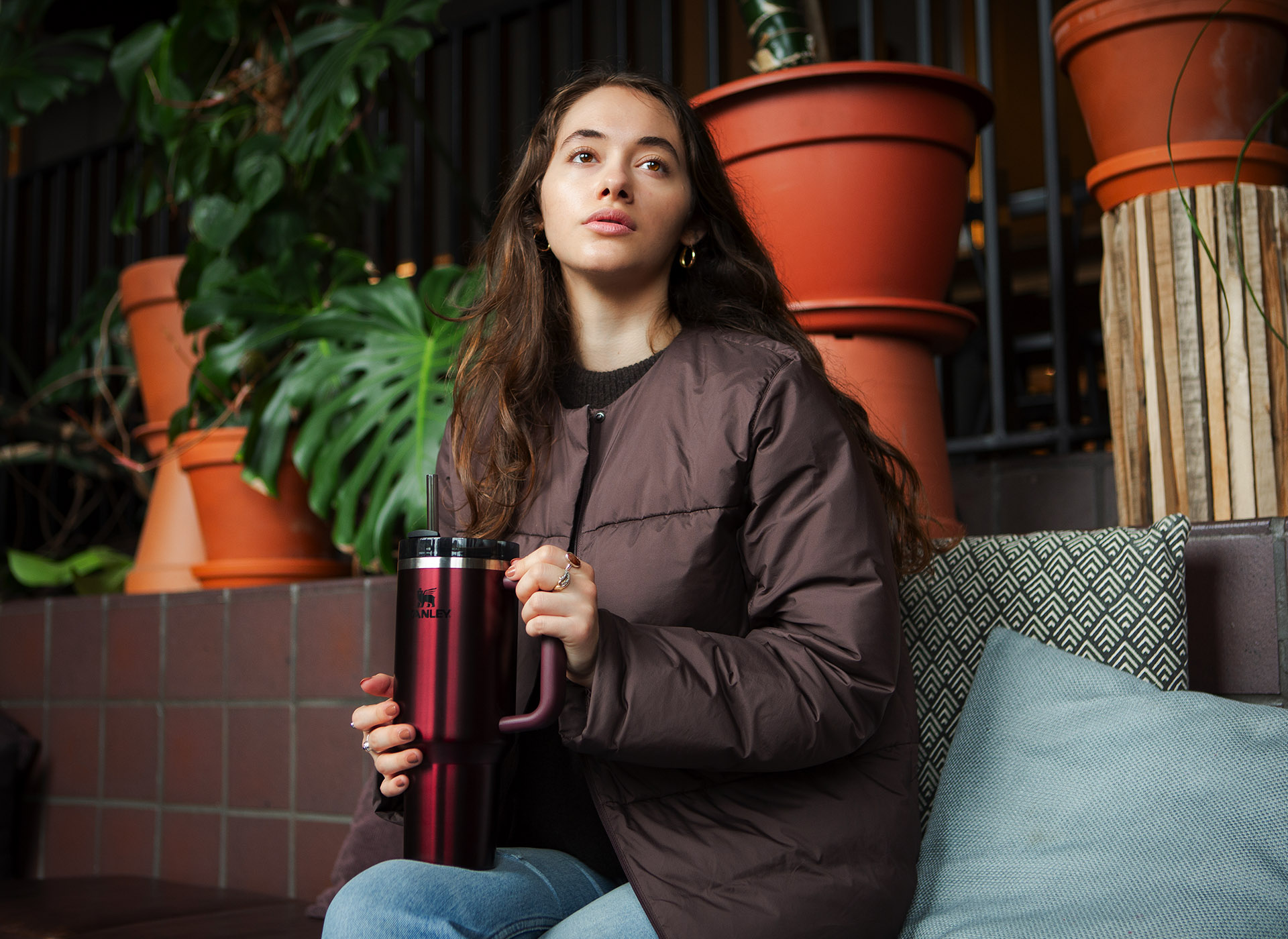 Woman sat indoors surrounded by indoor plants. She is holding a Stanley Glow Quencher