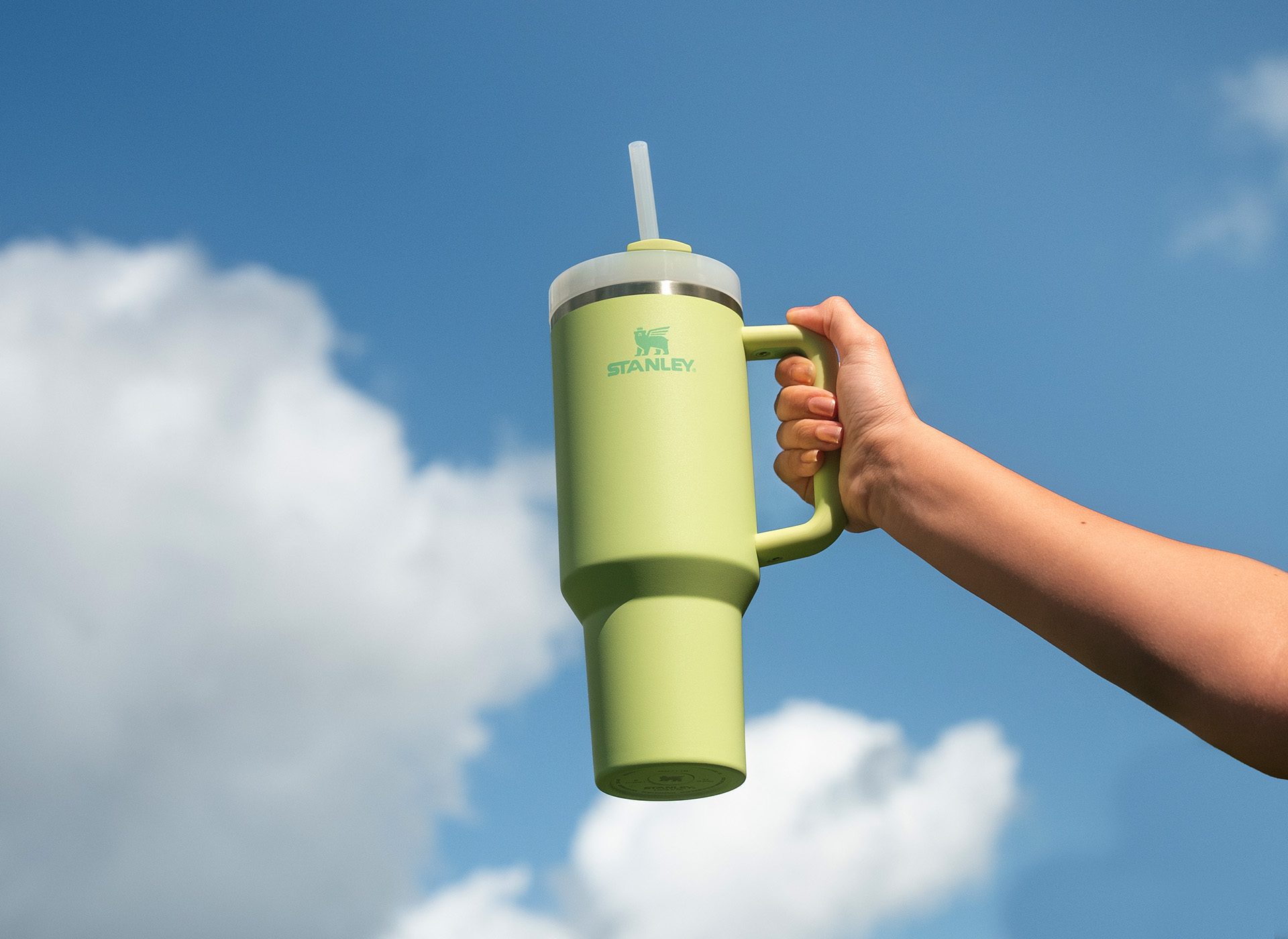 Hand holding citron Quencher in front of cloudy blue sky