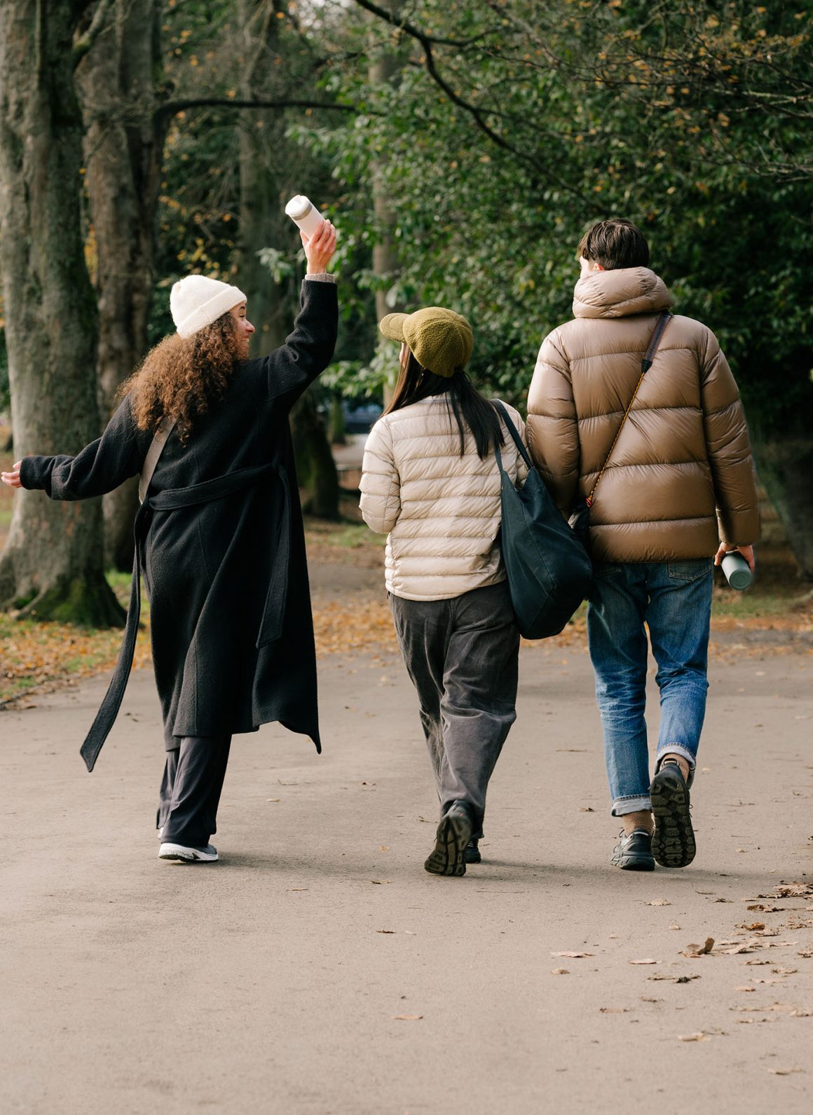 Shot of three people walking away from camera. The woman on the left is raising her flask in the air jubilantly