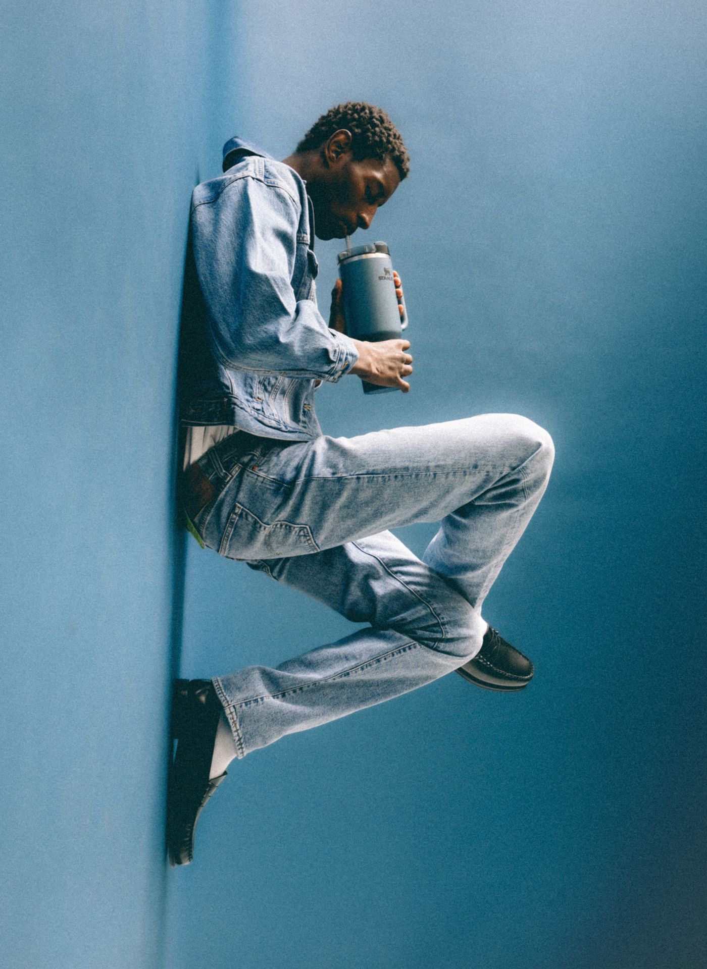 Image of man lying down in double denim outfit with Blue Spruce Stanley Quencher