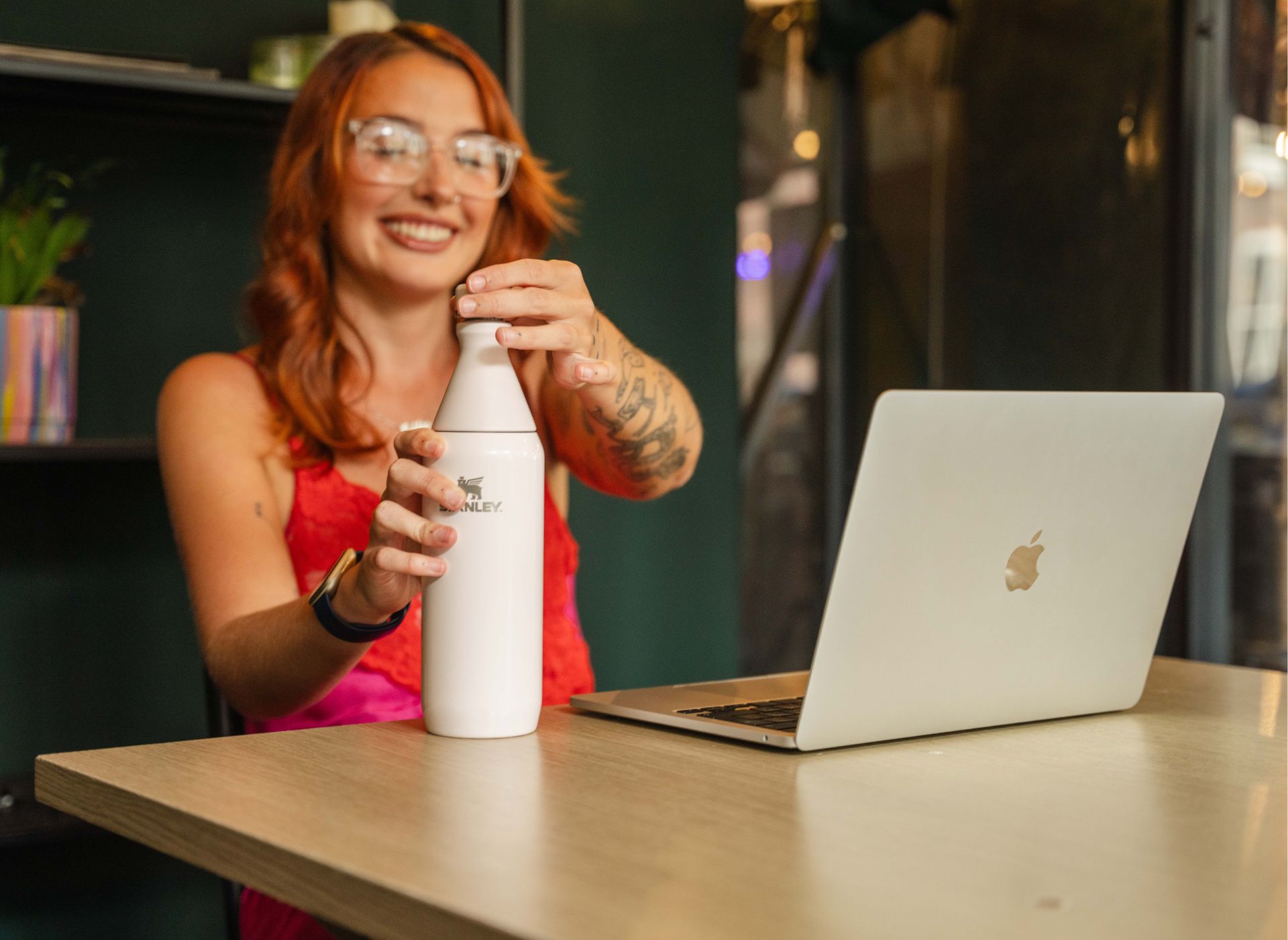 Ellie Middleton sitting with the All Day Slim bottle working from a cafe